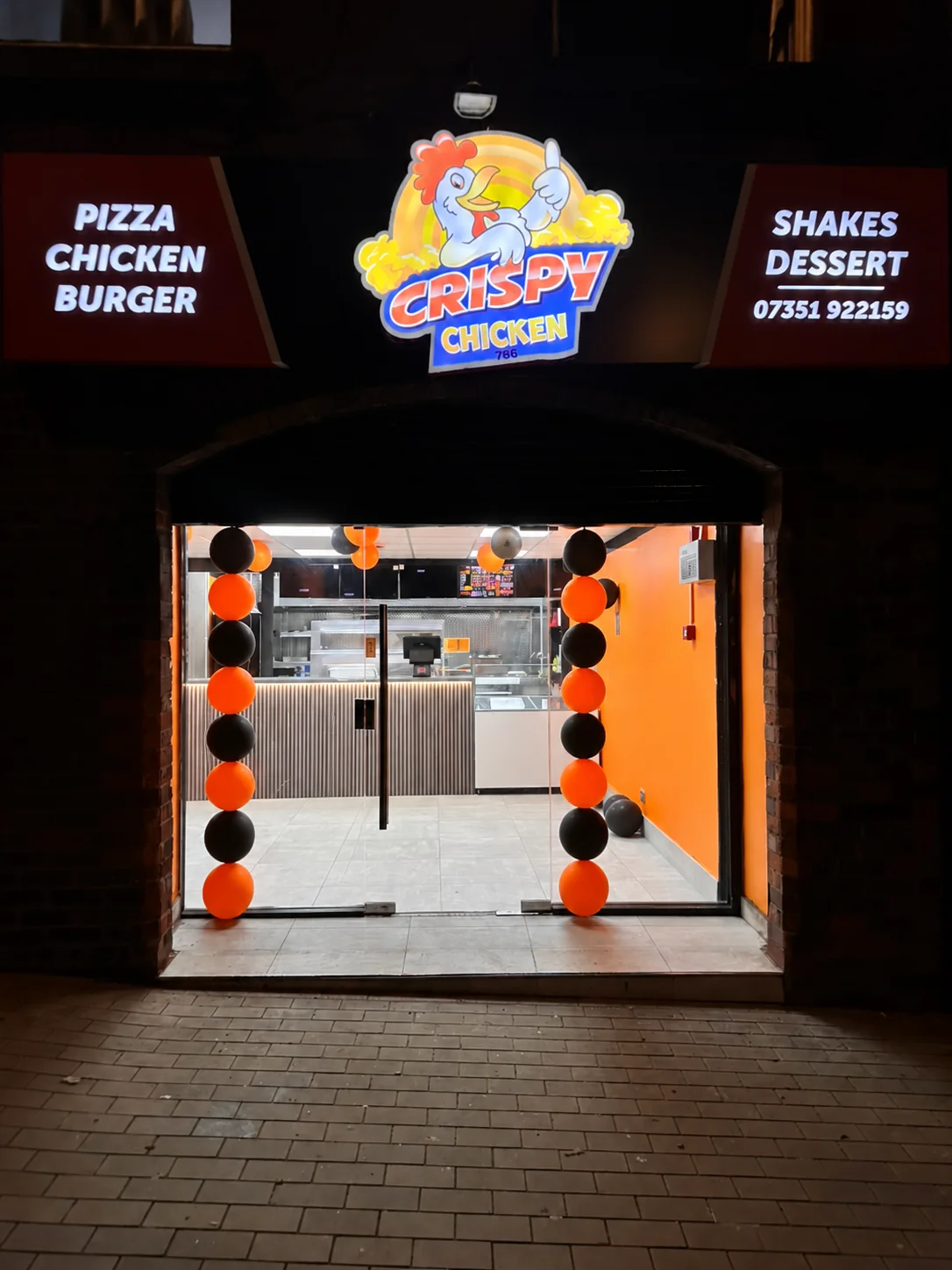Digitally enhanced photo of Crispy Chicken’s Middleton storefront at night, with orange and black balloon decorations.